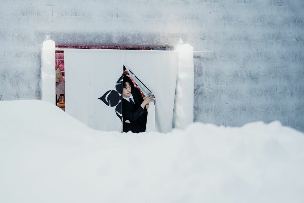 Authentic Japanese wedding moment with a guest entering through a noren curtain in snowy Hokkaido.