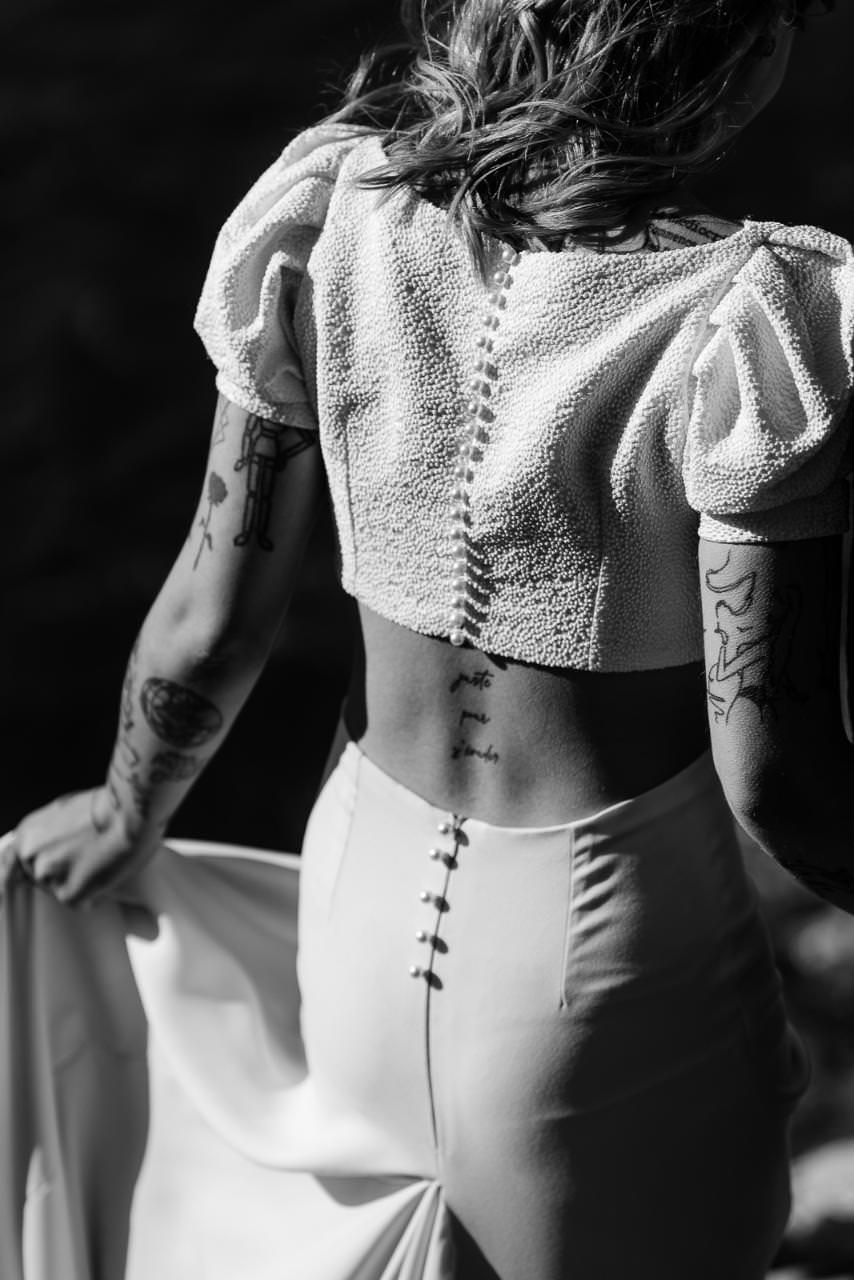 Black and white close-up of a bride’s back, showing button details and her modern bridal outfit.