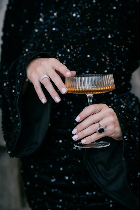 Editorial close-up of a woman holding a champagne coupe, showcasing luxury fashion details and jewelry at Palais de Tokyo in Paris.