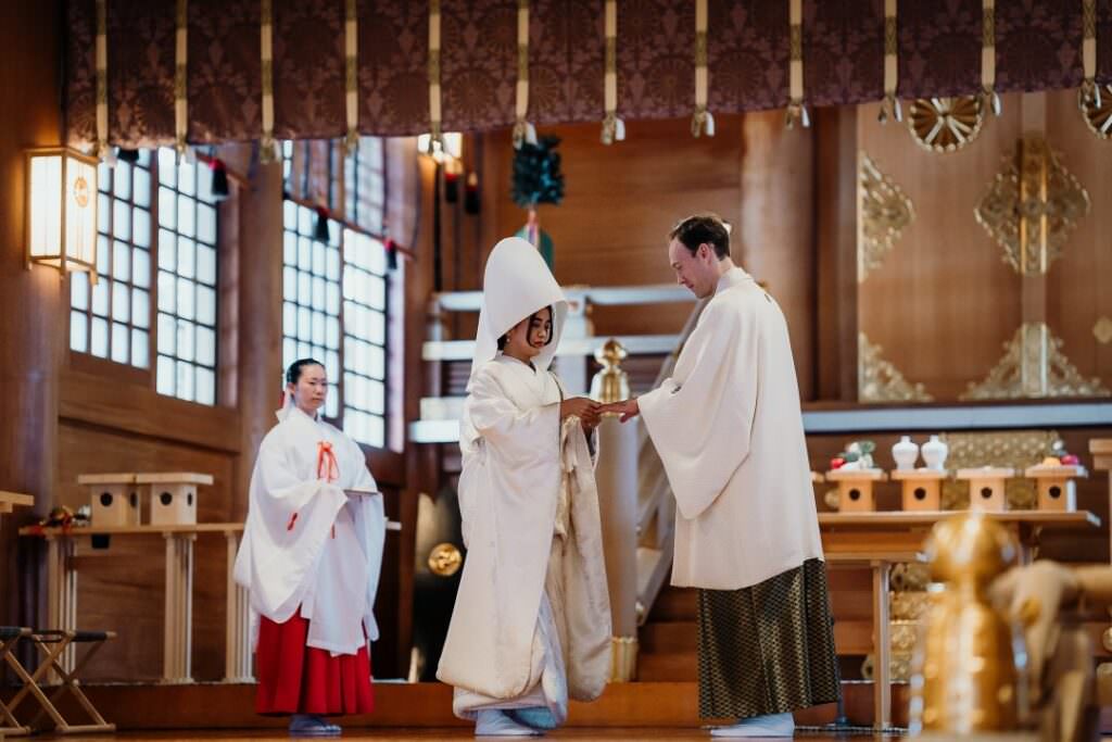 Elegant international couple taking part in a traditional ritual inside a Japanese Shinto shrine in Hokkaido.