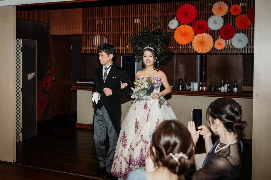Bride making a refined evening entrance with her father during an elegant destination wedding reception in Japan.