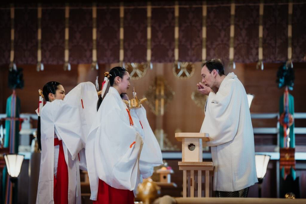 Elegant international couple sharing sake during the traditional san-san-kudo ritual in their Shinto wedding ceremony.