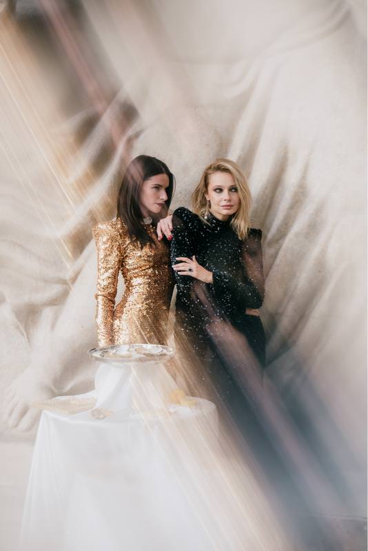 Fashion wedding editorial of two women in gold and black sequin gowns with prism light effect at Palais de Tokyo in Paris.