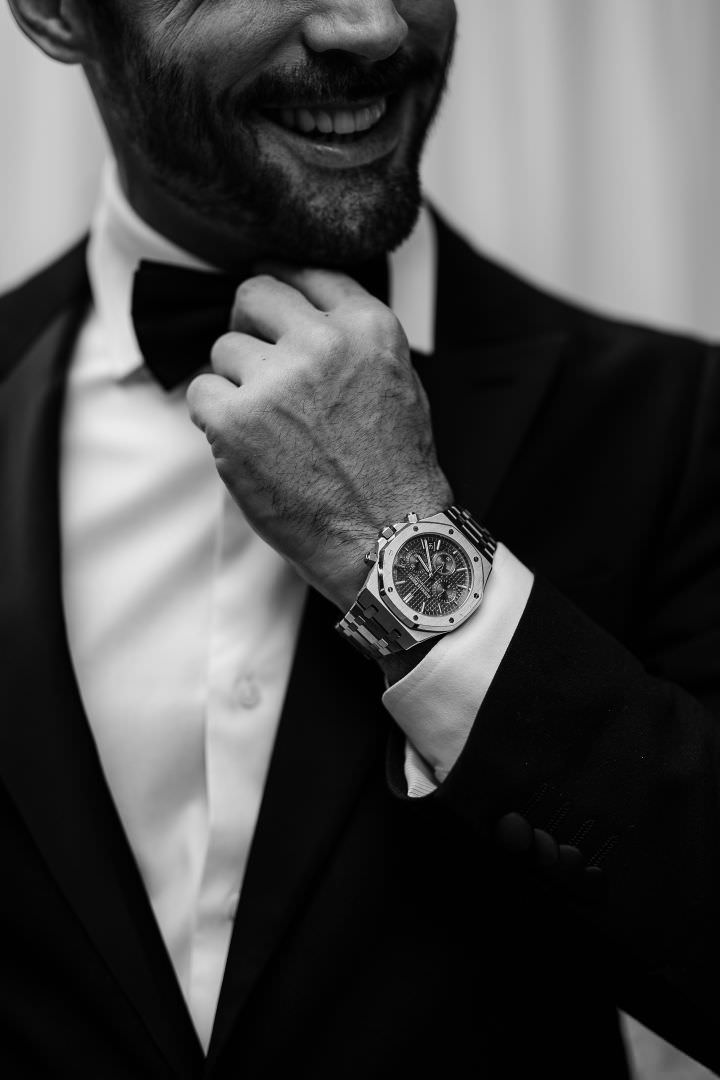 Refined black-tie groom adjusting his bow tie, captured in an elegant and editorial wedding portrait.