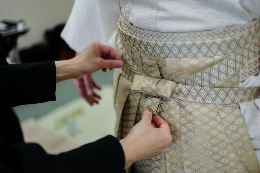 Hands adjusting the groom’s traditional montsuki hakama during wedding preparations.