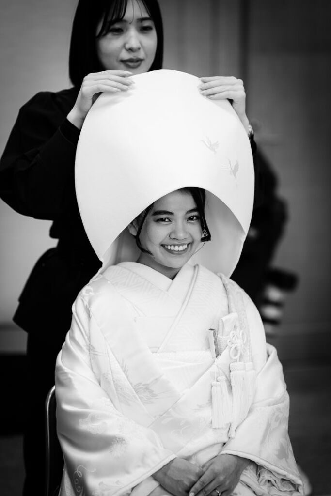 The bride being helped to put on her traditional watabōshi hood during Shinto wedding preparations in Hokkaido.