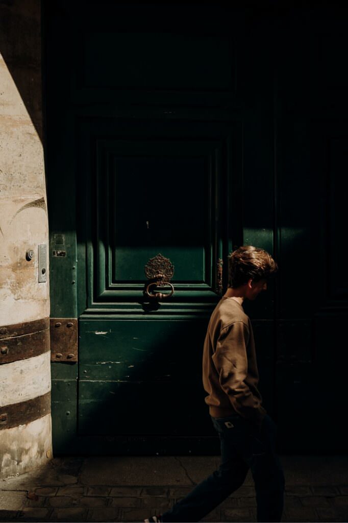 A man walking past a large wooden door, illuminated by a dramatic beam of natural light.