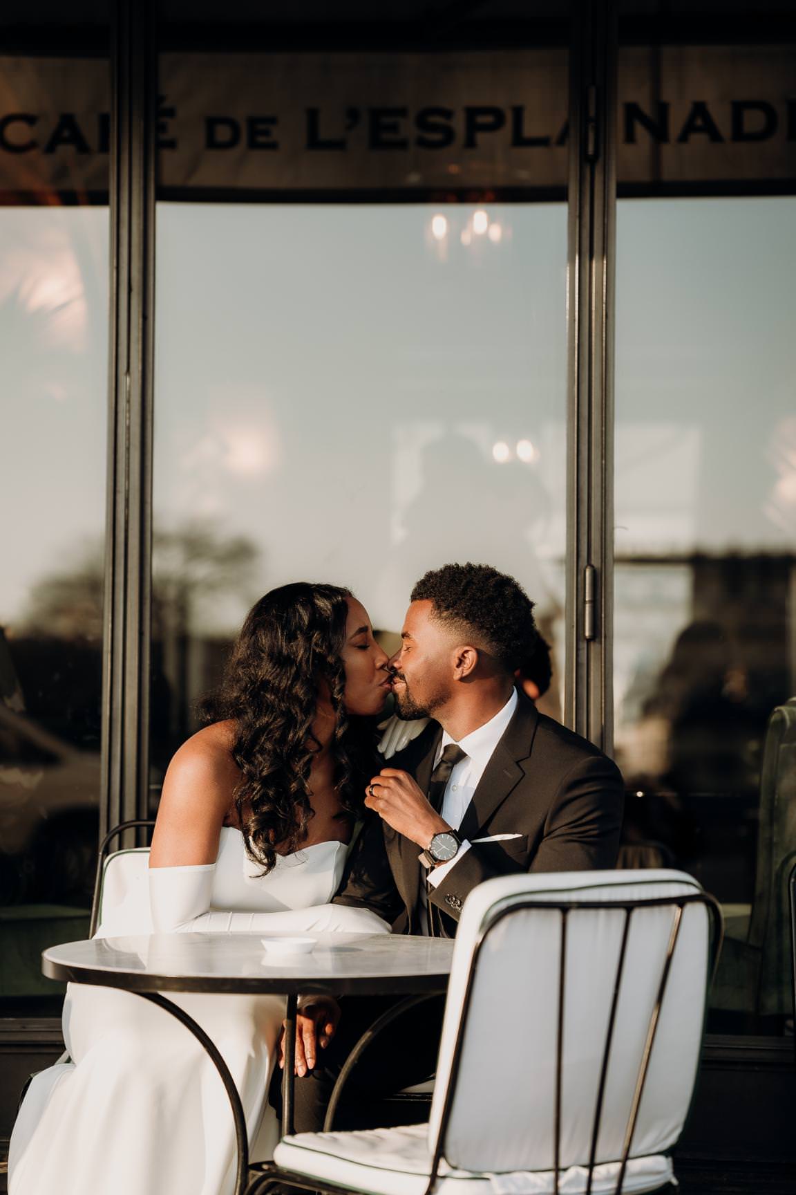 Romantic wedding couple sharing a kiss at a Parisian café in soft morning light.