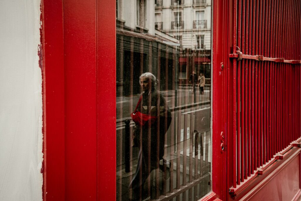 Street reflection of a woman in a red coat, framed by architectural lines.