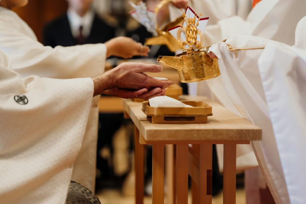 Detail of the san-san-kudo ritual with the couple’s hands exchanging ceremonial sake during their elegant Japanese wedding.