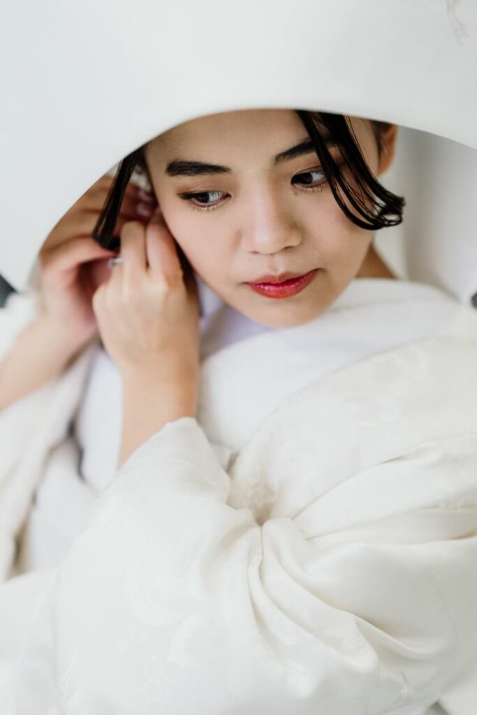 Close-up of the bride in a white shiromuku kimono adjusting her earring during her Japanese wedding preparations.