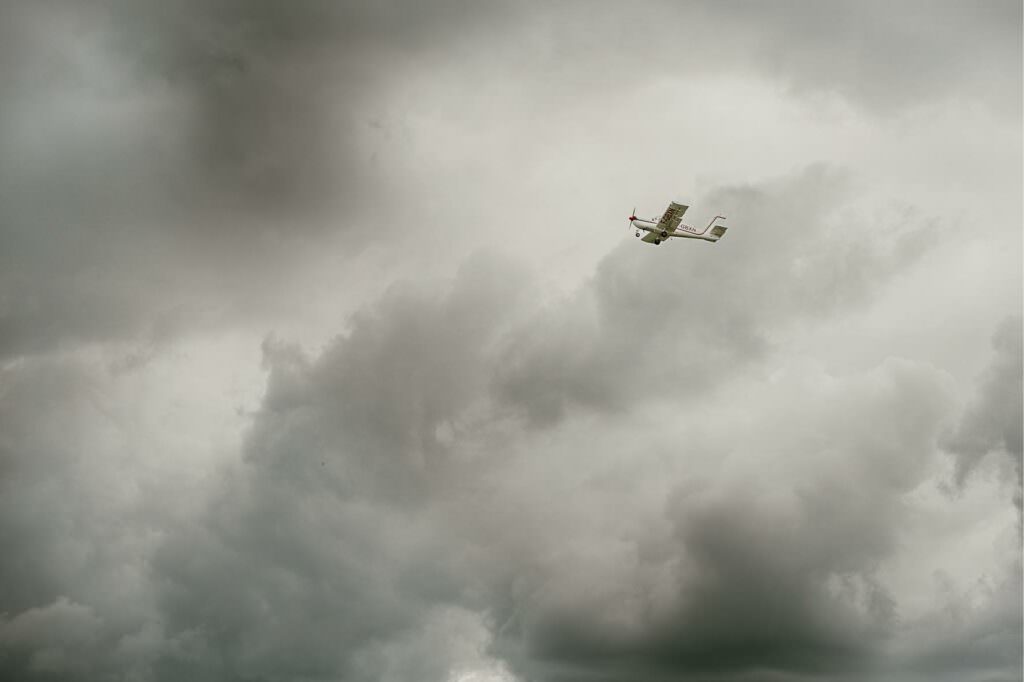 A small plane flying through a dramatic cloudy sky illuminated by soft storm light.