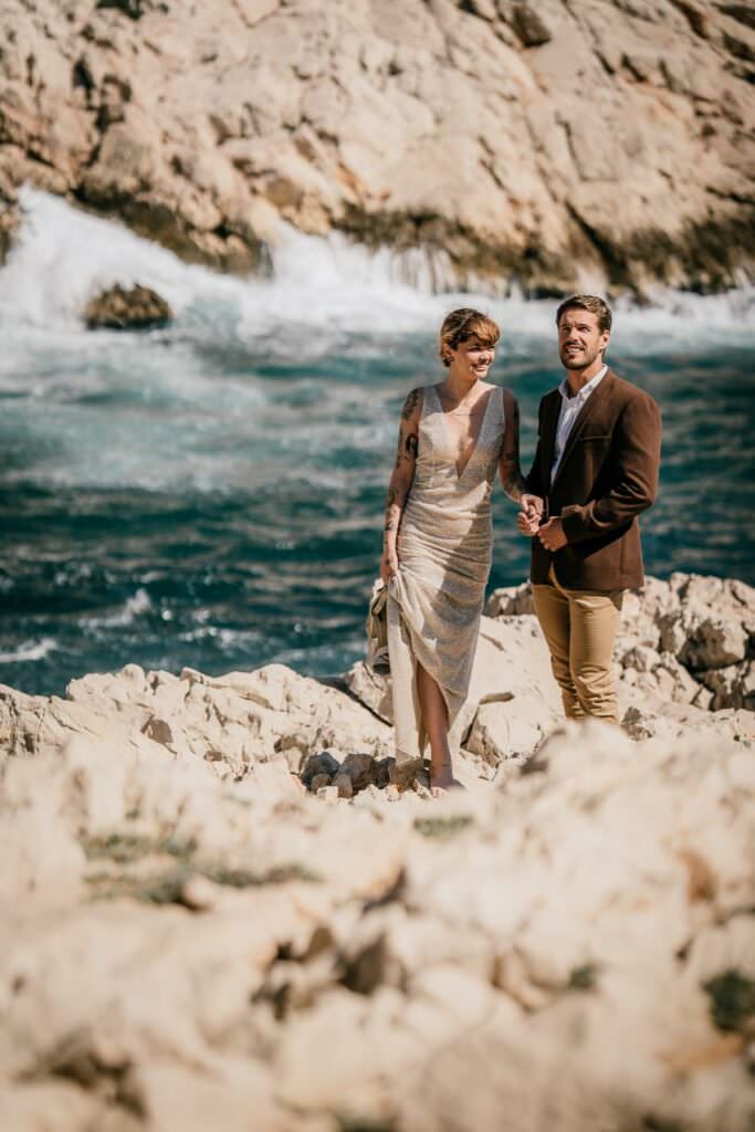 A couple walking hand in hand on seaside rocks during a South of France wedding, in warm natural light.