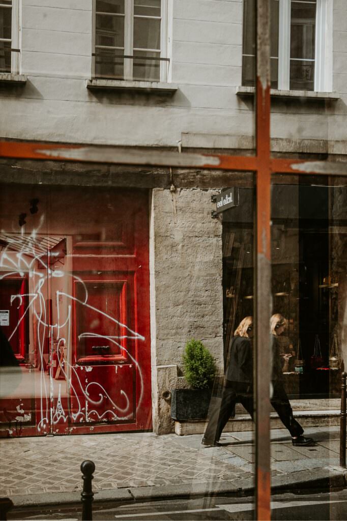 Paris street reflection in a shop window with subtle red architectural accents.
