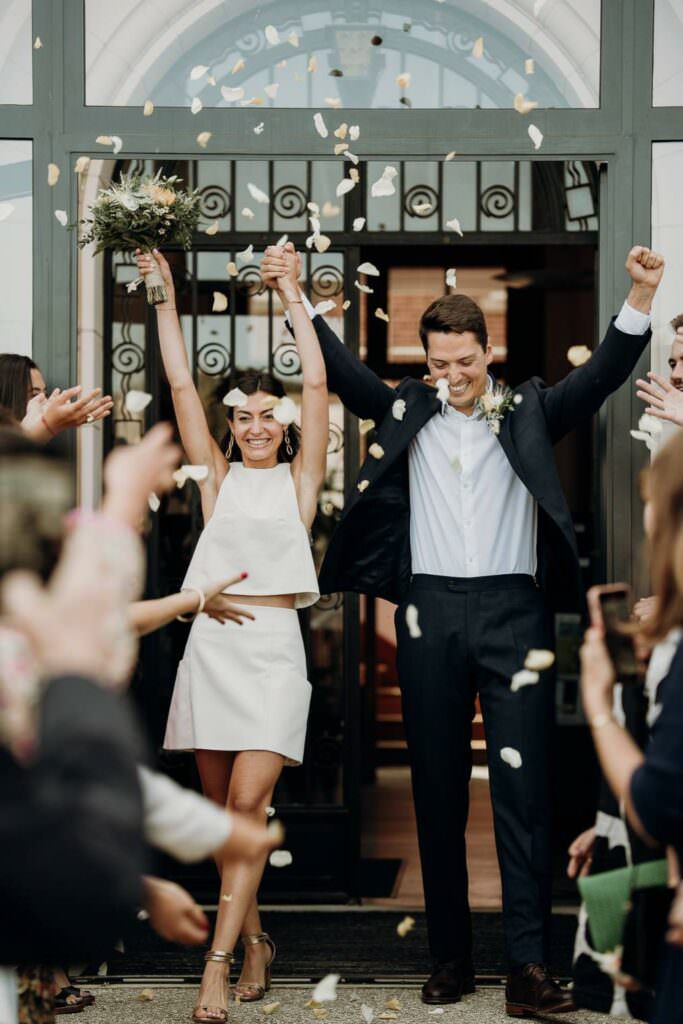 Joyful wedding ceremony exit with a stylish couple celebrating under falling petals.