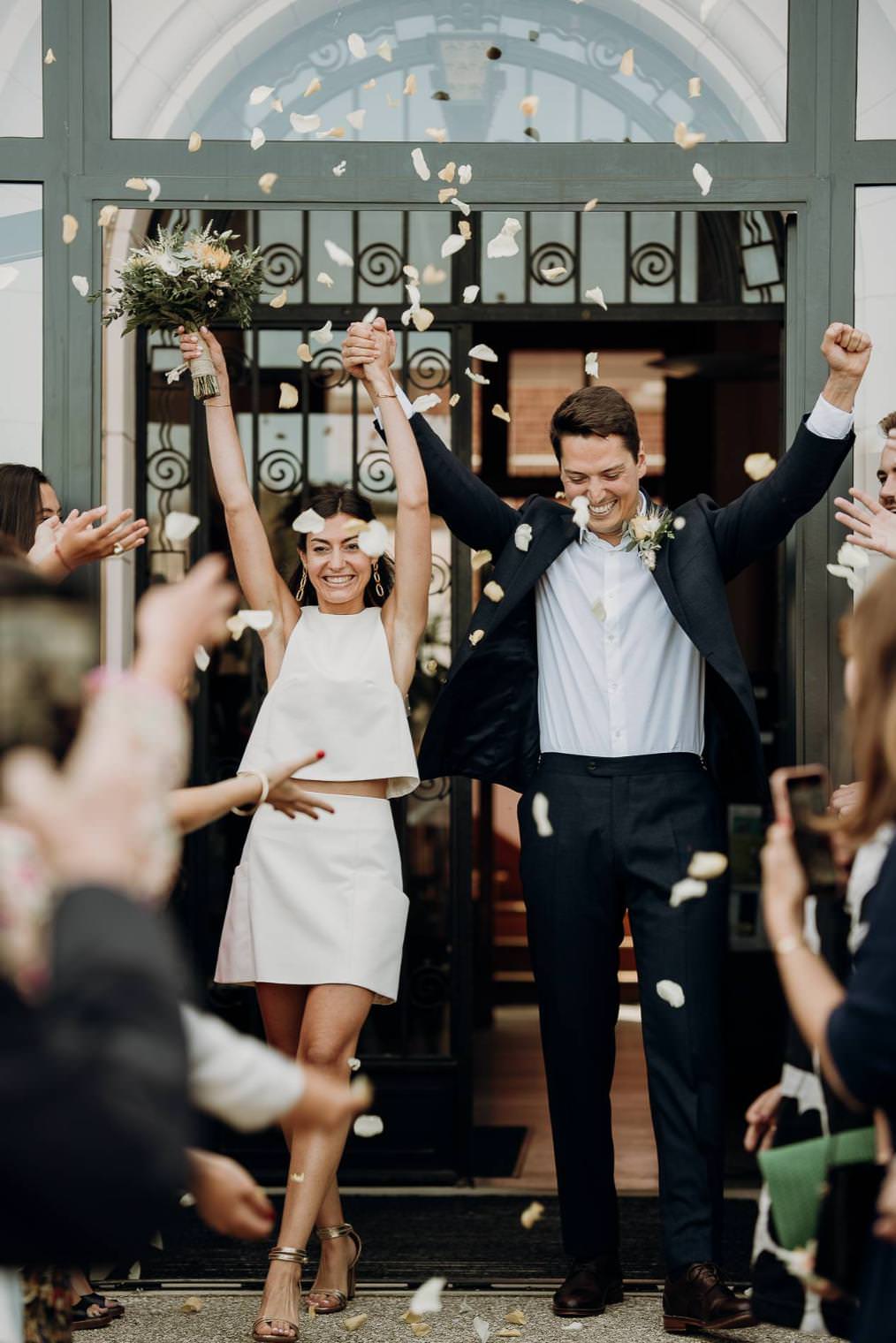 Joyful wedding ceremony exit with a stylish couple celebrating under falling petals.