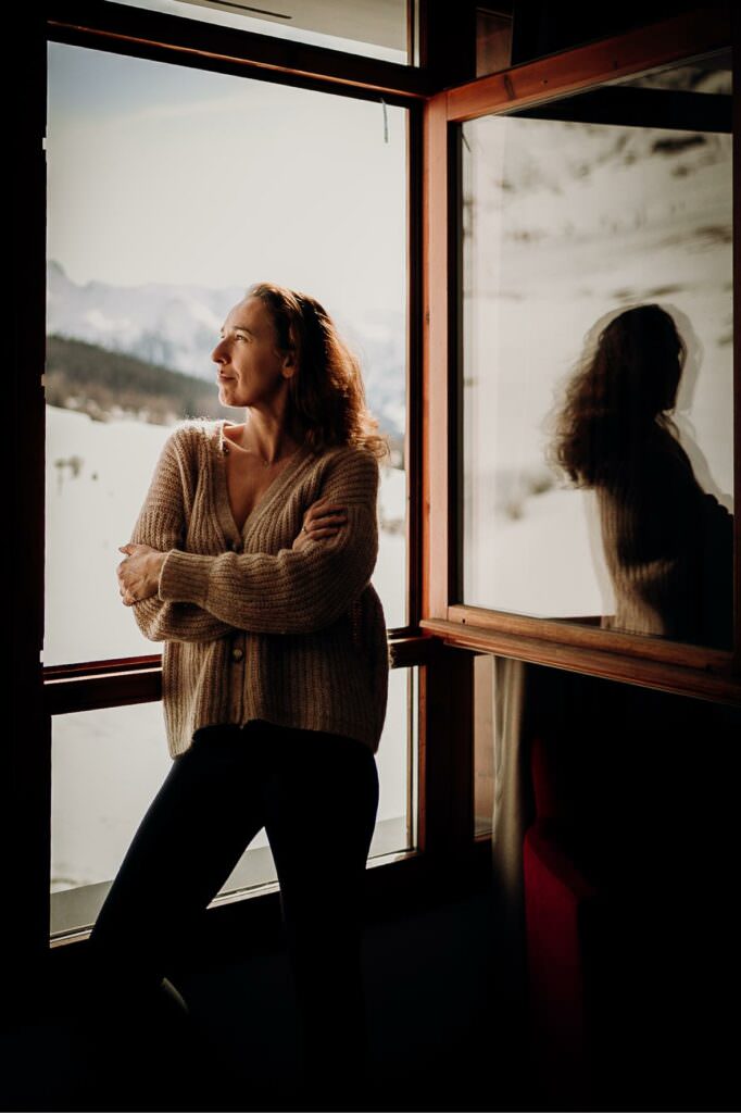 Soft portrait of a woman standing by an open window, bathed in natural light with a gentle reflection.