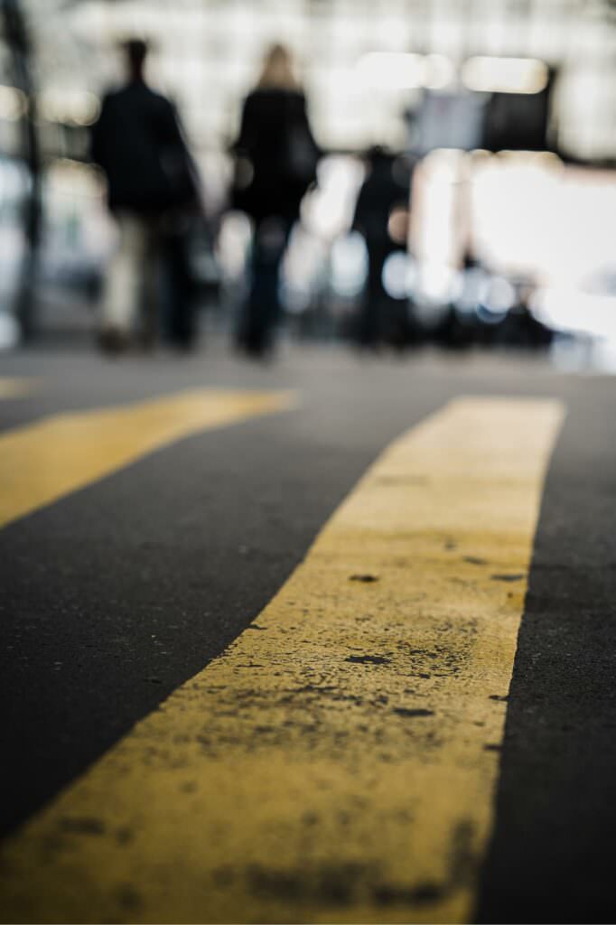 Yellow street lines in sharp focus with blurred pedestrians in the background.