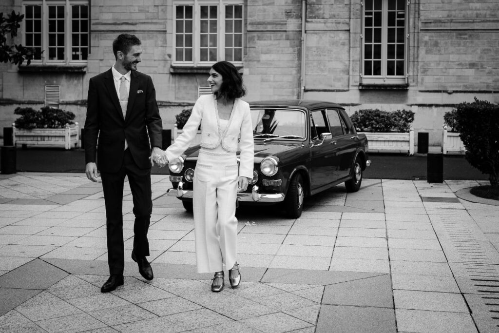 Bride and groom walking hand in hand beside a vintage car after their city hall wedding in Neuilly-sur-Seine